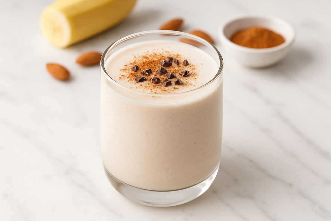 A creamy hormone-balancing maca energy smoothie in a clear glass with a light white color and subtle beige tint, topped with cinnamon and cacao nibs, photographed on a white marble surface with natural lighting and fresh ingredients in the background.